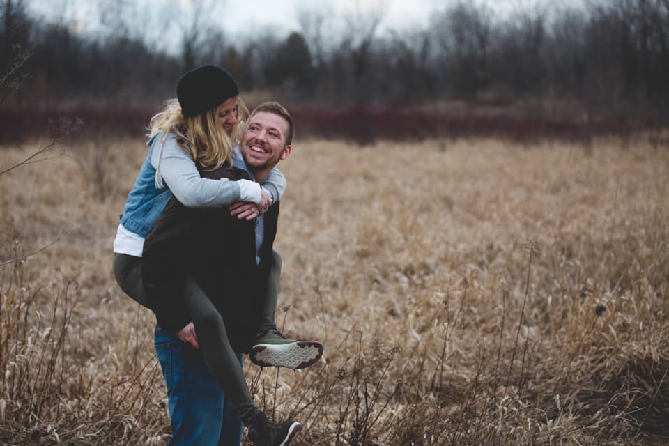 Groom giving the bride a piggyback through tall grass