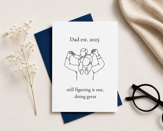 Greeting card with father and baby illustration and text on a light surface with decorative elements.